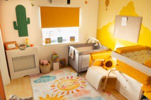 Bright and calming baby room at Little Lion Cubs Nursery in Netherfield, Nottingham, featuring a cosy cot, changing area, soft play rug, and warm yellow décor designed for under-2s.